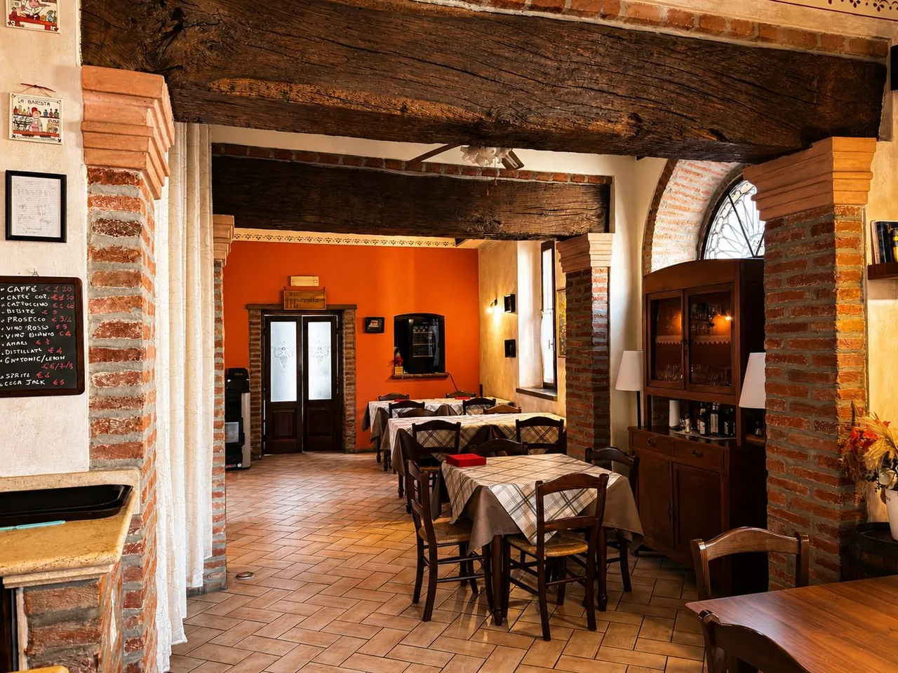 Sala dell'Osteria Il Ganascino con travi in legno, archi in mattoni e tavoli apparecchiati.