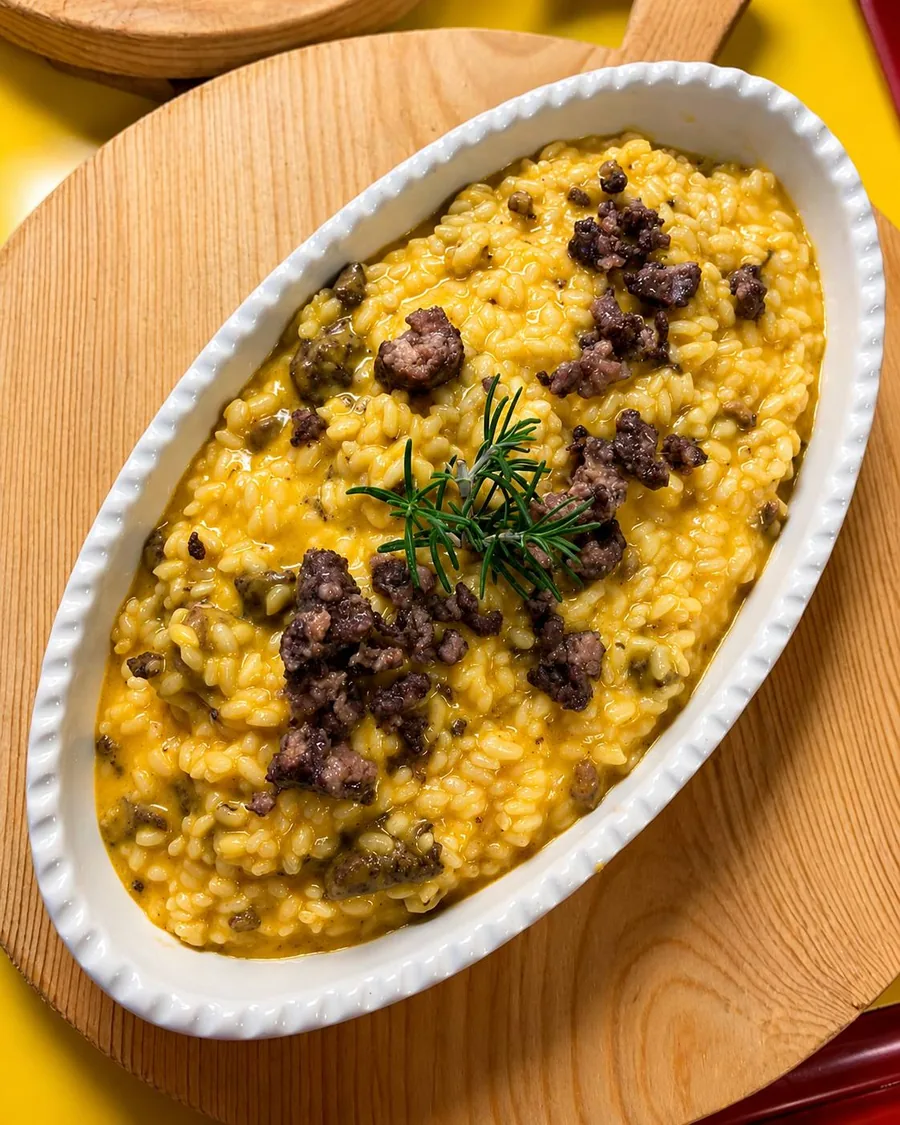 Risotto giallo servito in pirofila con salsiccia e rosmarino.